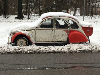 Snow covered car parked against trees during winter