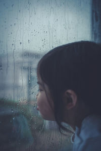 Close-up portrait of woman looking through wet window in rainy season