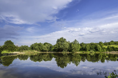 Scenic view of trees reflected to lake water at countryside in europe against summer dramatic sky