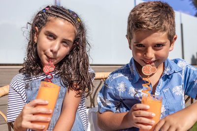 Two cute kids drinking orange juice outdoors