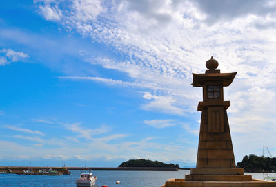 Lighthouse in sea against cloudy sky