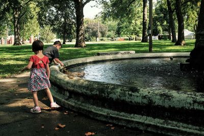 Cute brother and sister playing near pond in park against trees