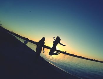 Silhouette people jumping on sea against clear sky