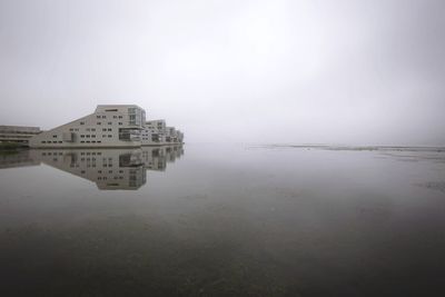 Reflection of buildings in lake against sky in city