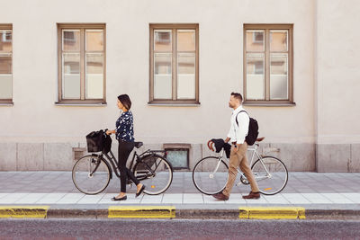 Side view of business colleagues walking with bicycles on sidewalk