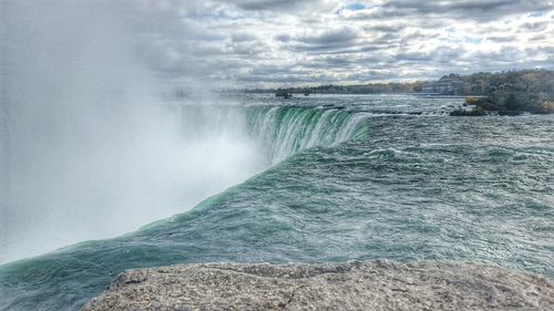 Water splashing on rocks against cloudy sky