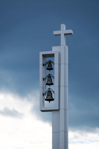 Low angle view of bells and religious cross on pole against sky