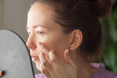 Young woman looking in the mirror and applying moisturizing face cream or lotion. skin care concept