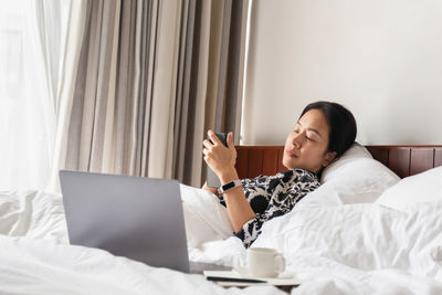 Woman using cell phone and laptop in bed 