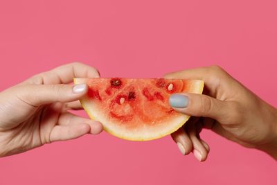 Close-up of hand holding apple against pink background