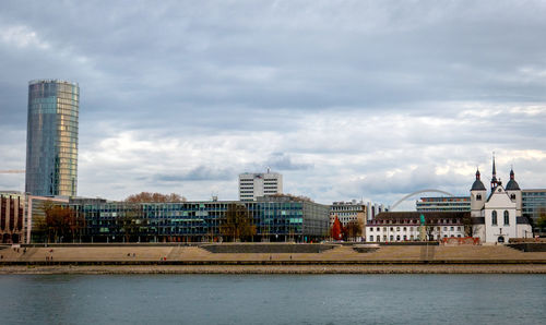 Buildings by river against sky in city