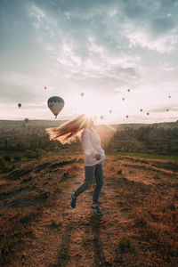 Rear view of man with balloons in field against sky