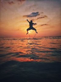 Silhouette man jumping at beach against sky during sunset
