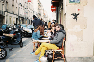 People at sidewalk cafe by street amidst buildings