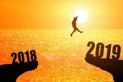 Silhouette of young man jumping between 2018 and 2019 years with beautiful sunset at the sea