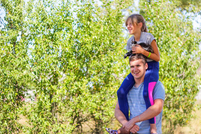 Brother riding sister on back. portrait of happy girl on man shoulders, piggyback. girl holding cat, 