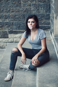 Portrait of young woman blowing gum while sitting on steps