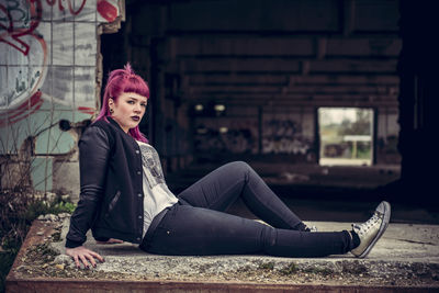 Portrait of young woman sitting by abandoned building