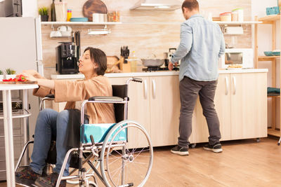 Disabled woman sitting on wheel chair in kitchen at home