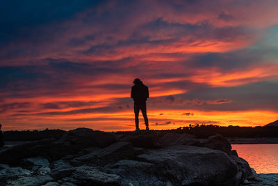 Rear view of silhouette man standing on rock against sky during sunset