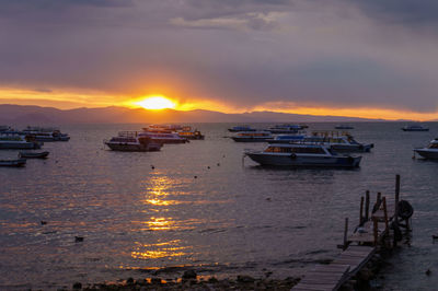 Sailboats moored on sea against sky during sunset