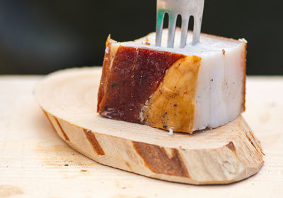 Piece of lard or bacon skewered with a fork on a wooden cutting board, close up