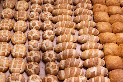 Various types of bread buns displayed orderly on top of a wooden display stand 