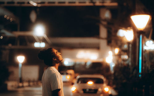 Rear view of man looking at illuminated street at night