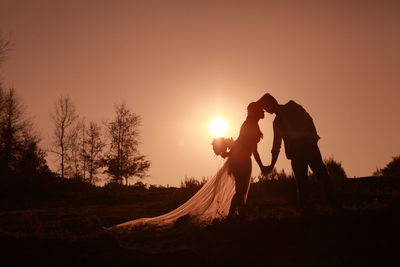 Silhouette bride and bridegroom standing against orange sky