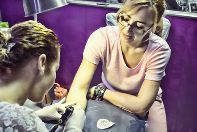 Female artist making tattoo on hand of woman