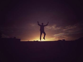 Silhouette men jumping against cloudy sky