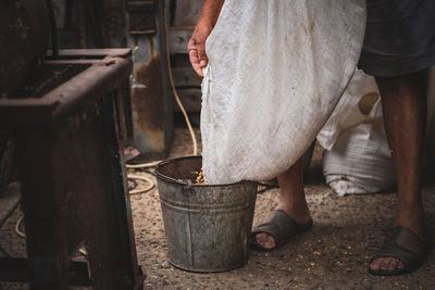 An elderly man pours wheat from a bag into a bucket.