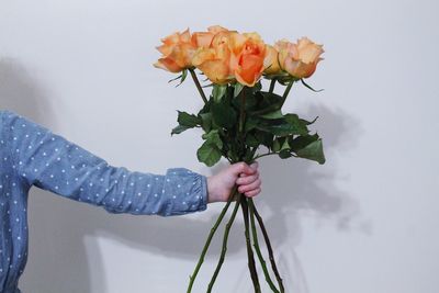 Cropped hand of woman holding bouquet against wall
