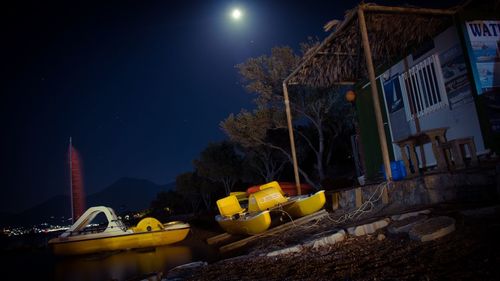 Yellow boat moored in river by built structure against sky at night
