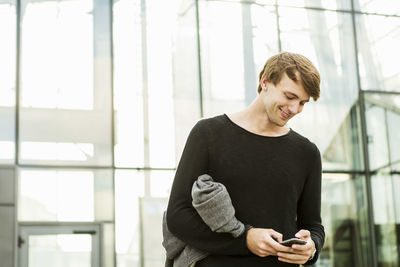 Smiling man using mobile phone while standing outside railroad station