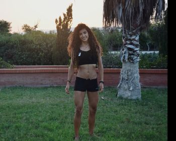 Portrait of young woman standing on grass against trees