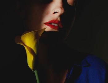 Close-up portrait of young woman with red lips and yellow calla lily over black background