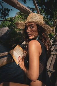 Midsection of woman holding hat while sitting outdoors