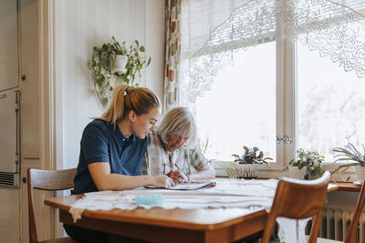 Female caregiver helping senior woman doing puzzle at home