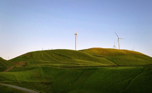 Windmills on green mountain against clear sky