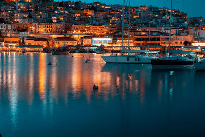 Sailboats in sea by illuminated city buildings