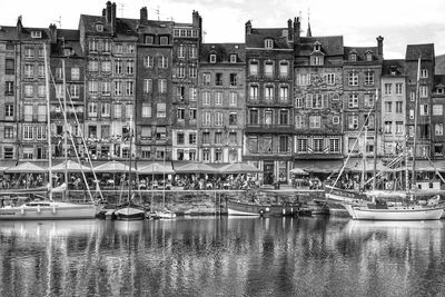 Sailboats in river by buildings against sky