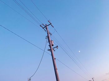 Low angle view of electricity pylon against clear blue sky