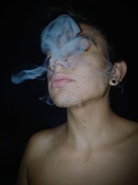 Close-up of young woman smoking over black background