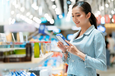 Woman holding smart phone while standing on laptop