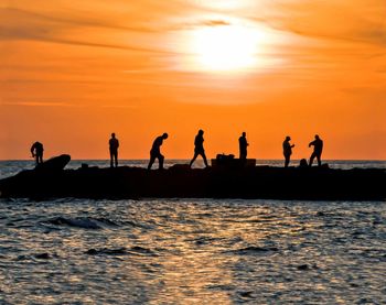 Silhouette people standing on beach against sky during sunset