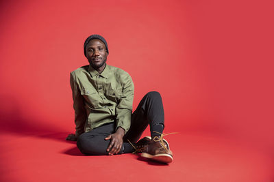 Portrait of young man sitting against red background