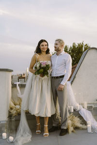 Portrait of smiling bride standing with groom near decoration on rooftop