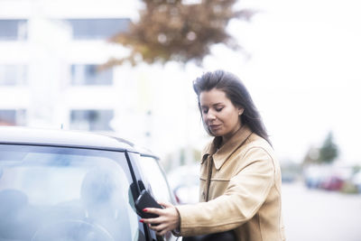 Young woman standing by car in city