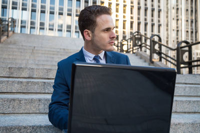 Businessman using laptop while sitting on steps in city